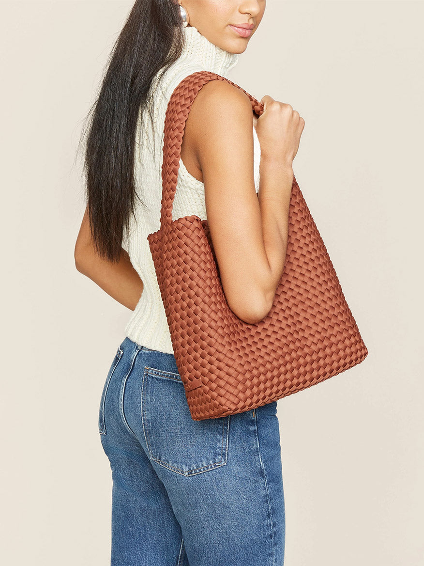 Woman carrying a Naghedi Nomad Hobo in Solid Adobe over her shoulder, dressed in casual attire with a sleeveless white top and blue jeans.