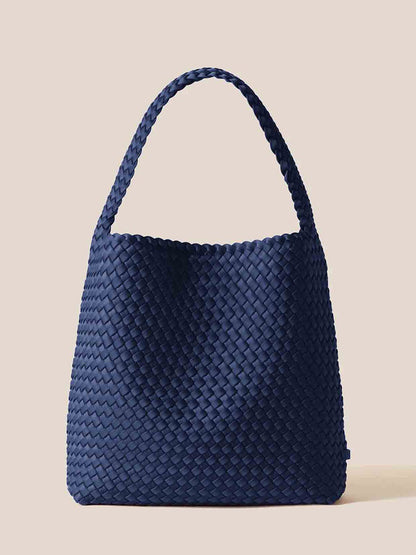 The Naghedi Nomad Hobo in Solid Ink Blue is a handwoven bag made from striking blue neoprene, featuring a single handle against a plain background. It's both spacious and comfortable, making it perfect for any journey.