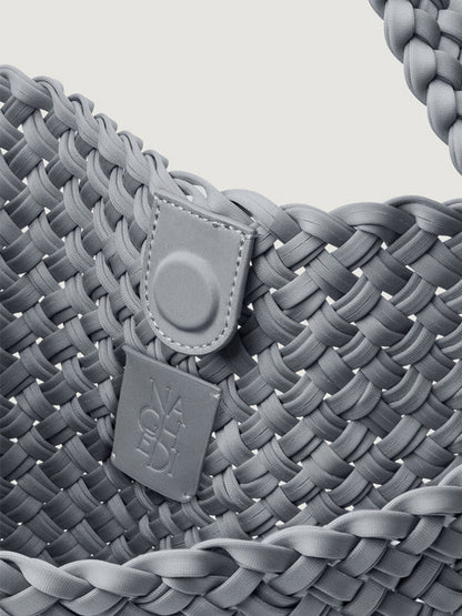 Close-up of a blue-grey Naghedi Nomad Medium Hobo Double Weave in Marina, a handwoven bag with a magnetic snap closure and a branded square tag.