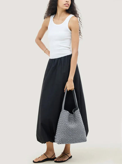 A person wearing a white tank top and a black maxi skirt, holding a grey Naghedi Nomad Medium Hobo Double Weave in Marina.