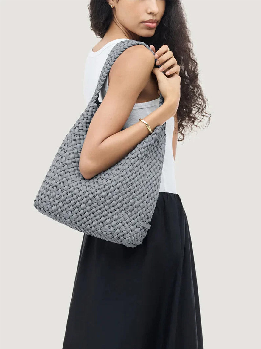 A person carries a gray Naghedi Nomad Medium Hobo Double Weave in Marina handwoven bag on their shoulder.