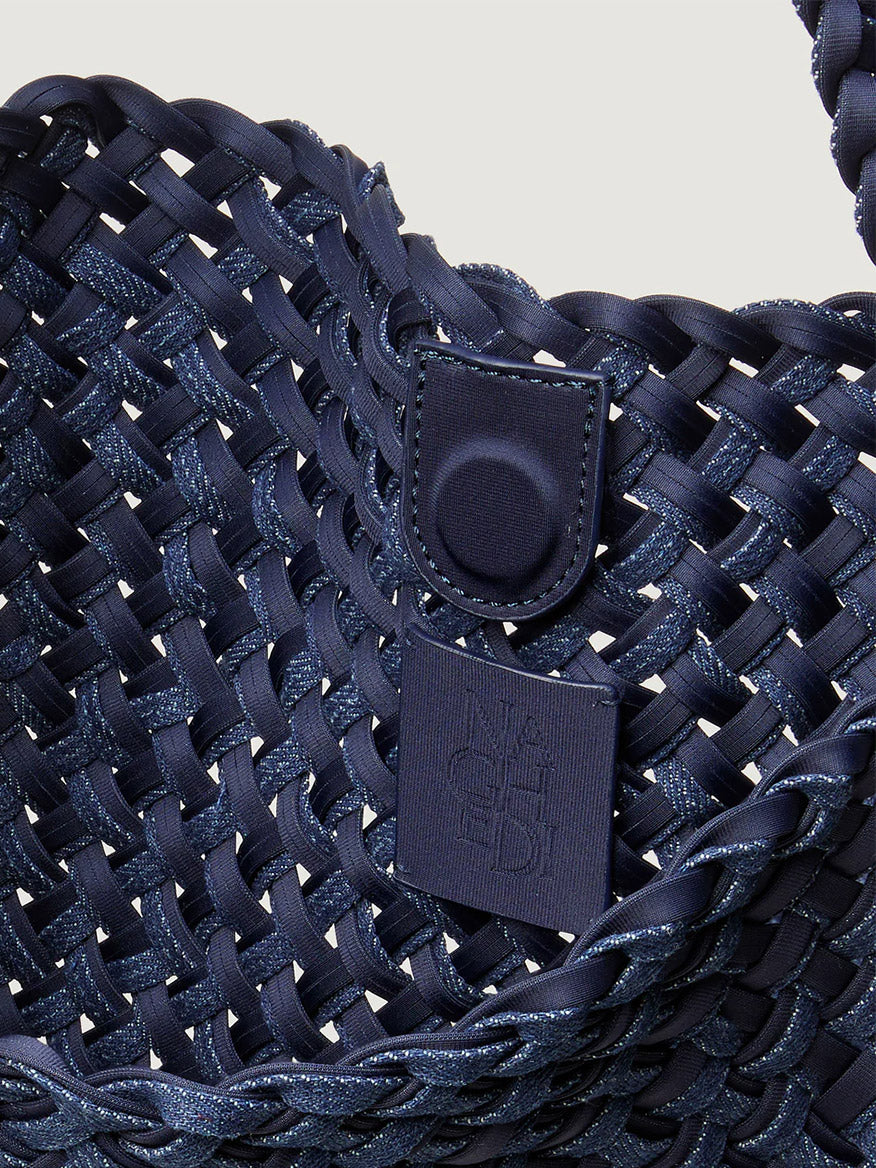 Close-up of the Naghedi Nomad Medium Hobo Double Weave Denim in Indigo, a spacious, lightweight handwoven bag with a magnetic snap closure and a square embossed logo patch.