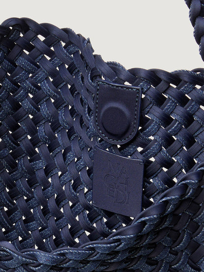 Close-up of the Naghedi Nomad Medium Hobo Double Weave Denim in Indigo, a spacious, lightweight handwoven bag with a magnetic snap closure and a square embossed logo patch.