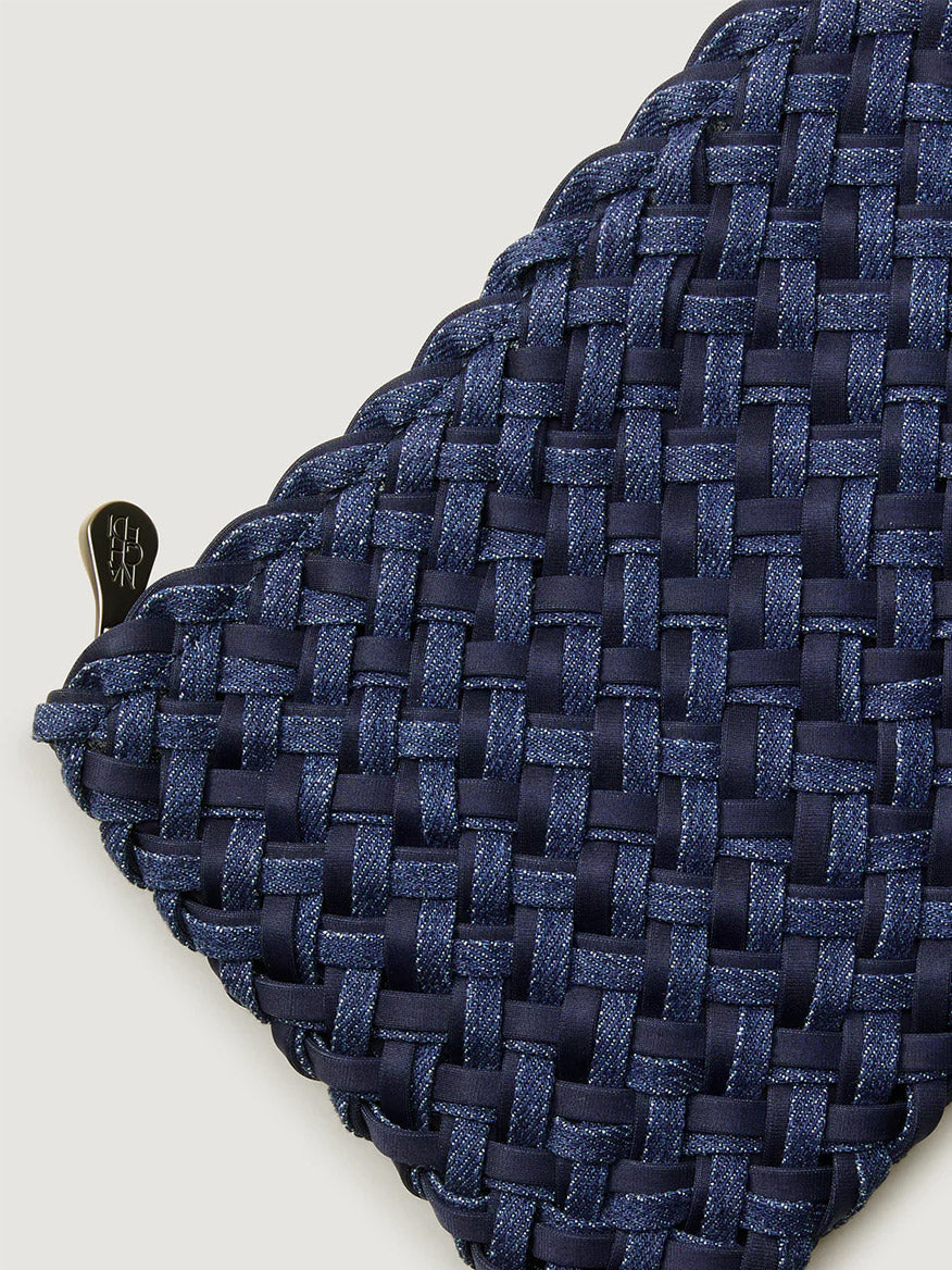 Close-up of the Naghedi Nomad Medium Hobo Double Weave Denim in Indigo, a triangular handwoven bag with a dark blue pattern and a small black metal clasp on the left side.