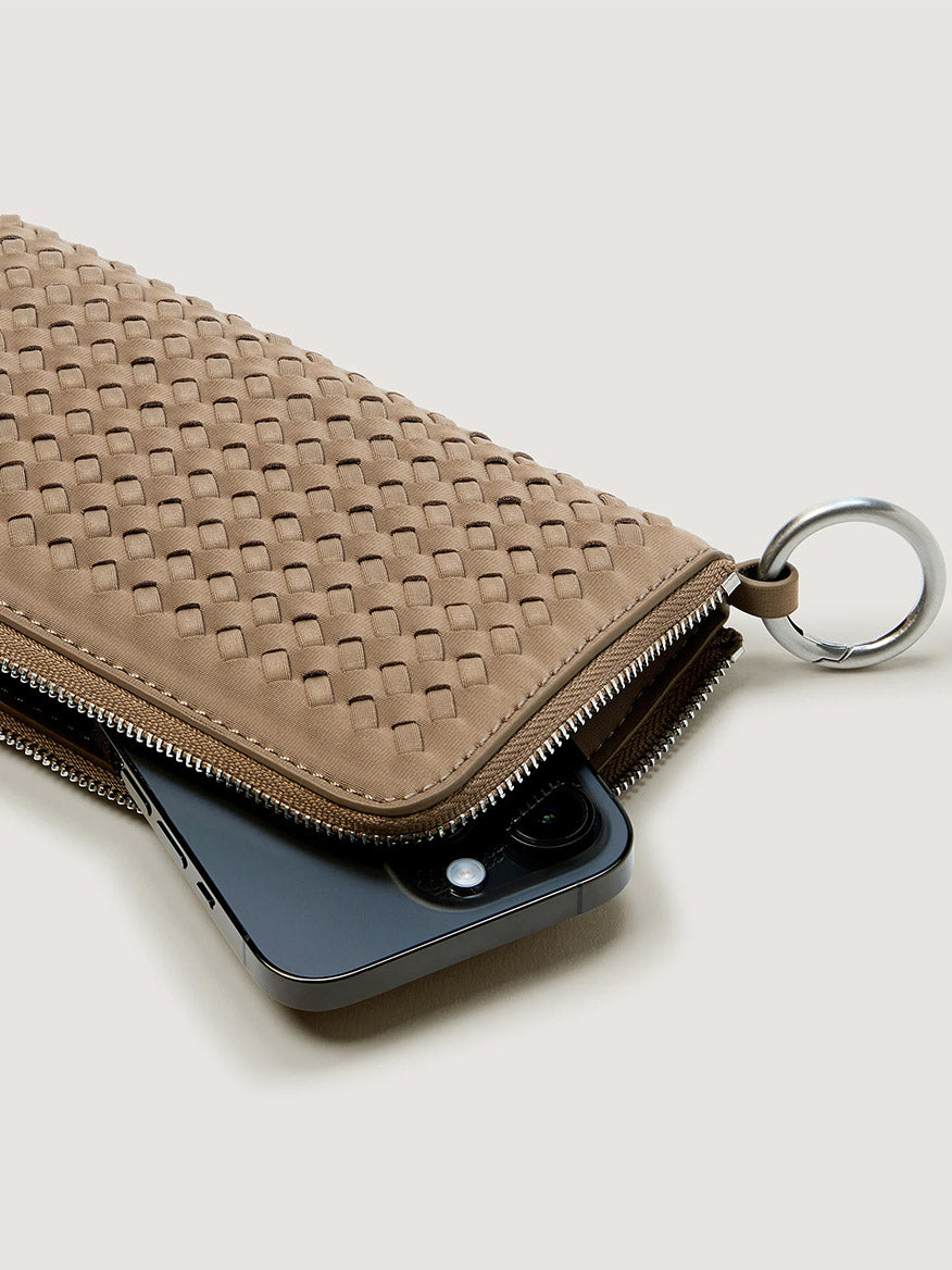 Naghedi Orly Phone Case in Cashmere, a taupe woven crossbody bag with a silver ring attachment, shown with a smartphone partially inserted into the minimalist pouch.