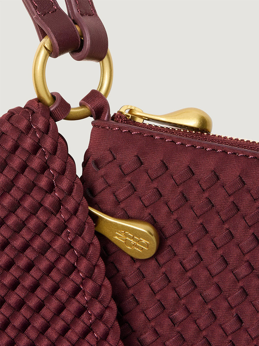 Naghedi Orly Phone Case in Bordeaux, a woven crossbody bag featuring gold-tone hardware, zipper pulls, and an adjustable leather strap.