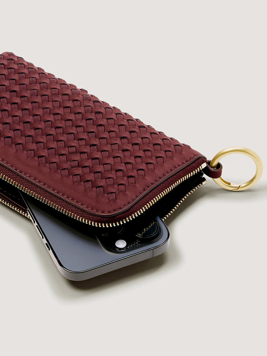 Naghedi Orly Phone Case in Bordeaux, a deep red woven zip-up minimalist phone pouch with a gold keyring attached.