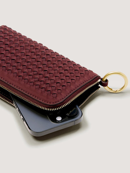Naghedi Orly Phone Case in Bordeaux, a deep red woven zip-up minimalist phone pouch with a gold keyring attached.