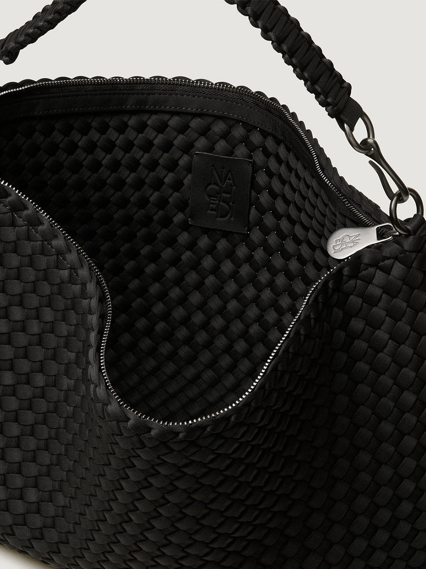 Close-up of the Naghedi Porto Medium Half-Moon Bag in Onyx, featuring an open handwoven design with zipper, textured interior, logo patch, and braided handle.