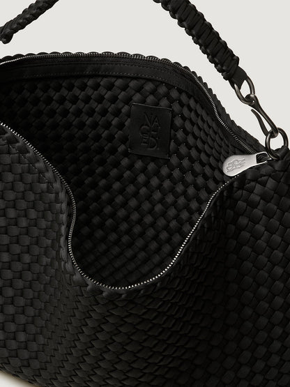 Close-up of the Naghedi Porto Medium Half-Moon Bag in Onyx, featuring an open handwoven design with zipper, textured interior, logo patch, and braided handle.