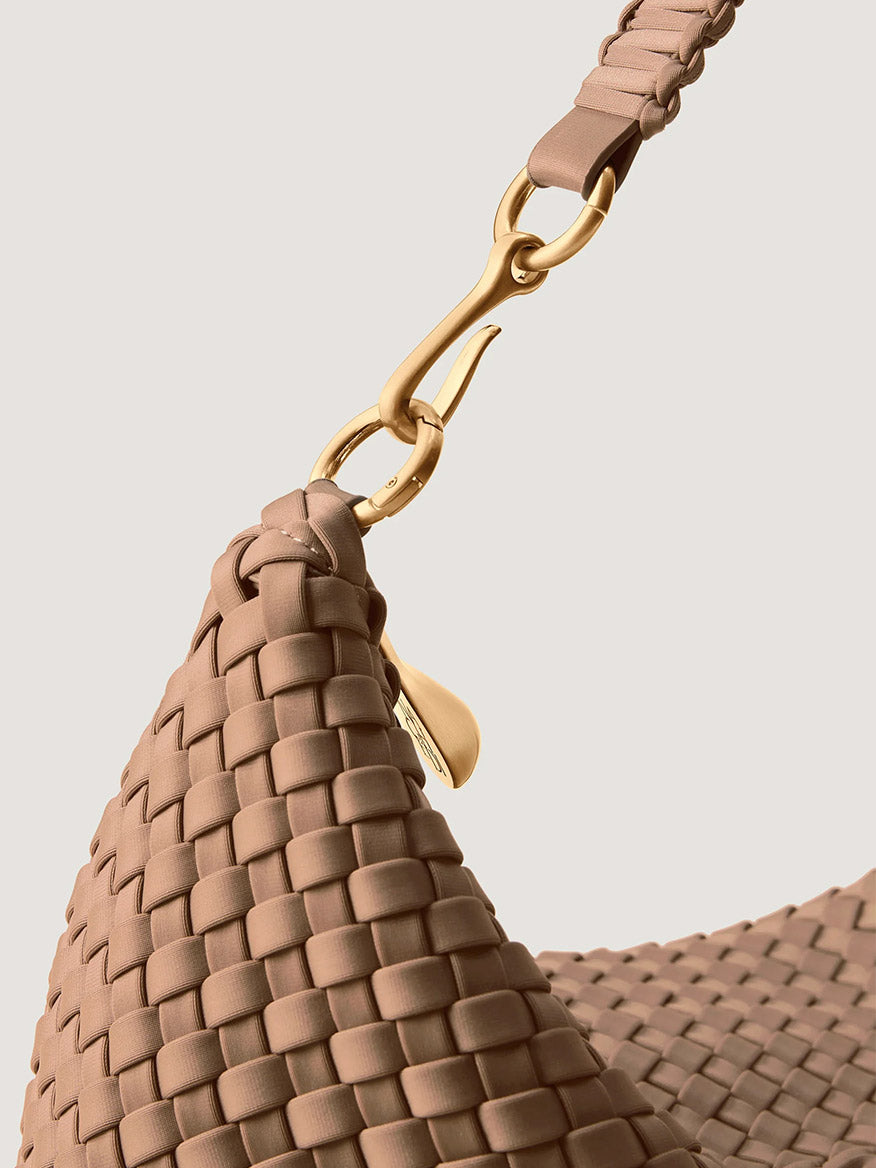 Close-up of a Naghedi Porto Medium Half-Moon Bag in Seychelles, a tan woven neoprene half-moon shoulder bag with a gold metal clasp and strap.