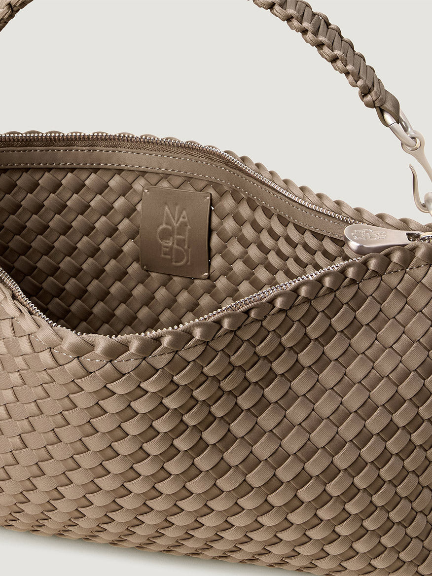 Close-up of a taupe, handwoven neoprene Naghedi Porto Medium Half-Moon Bag in Cashmere with a zippered top and interior brand patch.