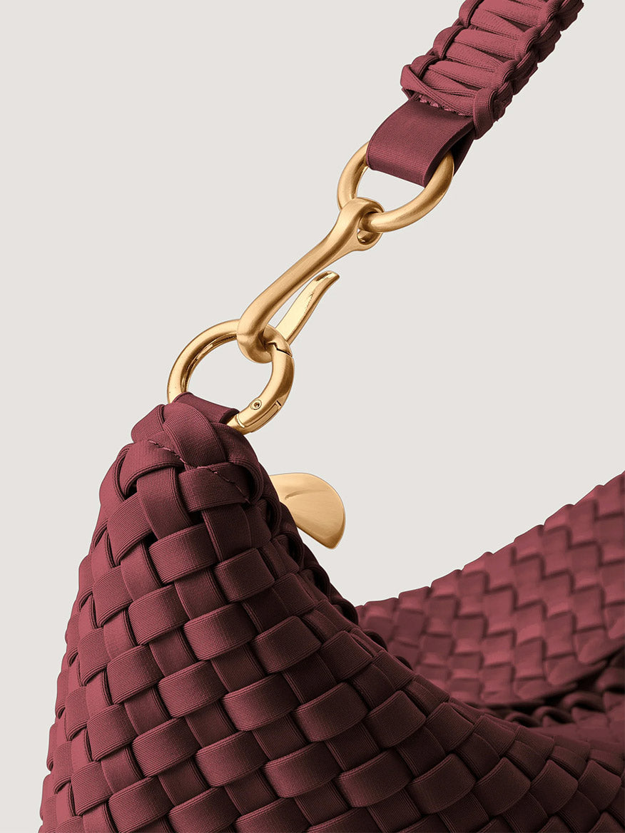 Close-up of a burgundy Naghedi Porto Small Half-Moon Bag with a gold metal clasp connecting the strap to the bag body.