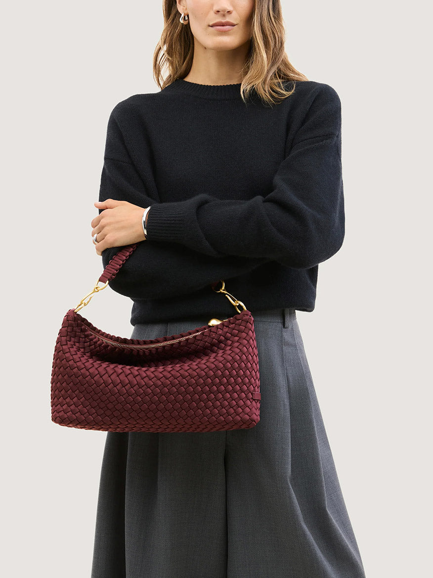 A person holds a deep red, handwoven Naghedi Porto Small Half-Moon Bag in Bordeaux with gold hardware.