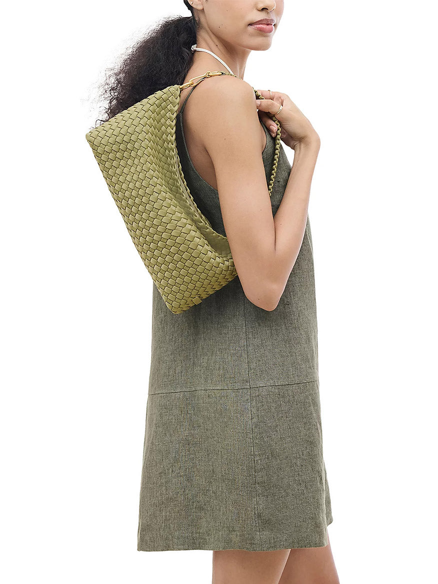 A person wearing a Naghedi Porto Small Half-Moon Bag in Bottle Green, a handwoven green shoulder bag.