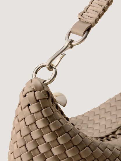 Close-up of a handwoven beige Naghedi Porto Small Half-Moon Bag in Cashmere with a braided strap and a metal swivel clasp.