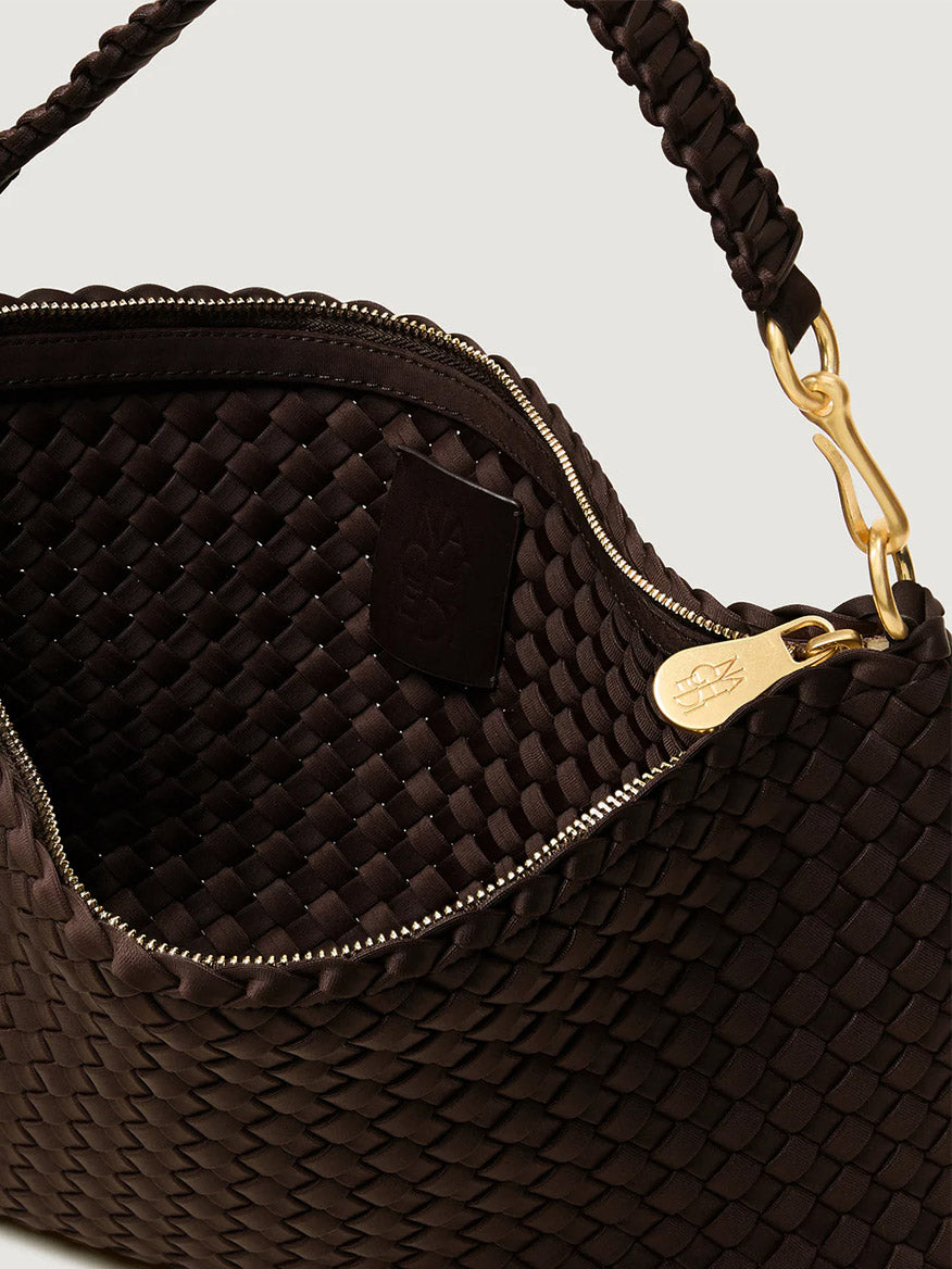 Close-up of the Naghedi Porto Small Half-Moon Bag in Chocolate, featuring handwoven neoprene, gold hardware, a braided handle, and zipper closure. Interior tag shown inside the open bag—ideal for day-to-night versatility.