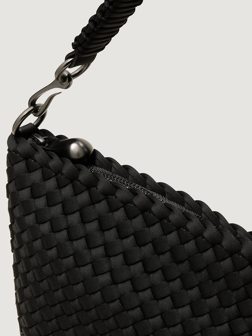 Close-up of the Naghedi Porto Small Half-Moon Bag in Onyx, a black handwoven neoprene bag with a zipper closure and a black metal clasp on the handle.