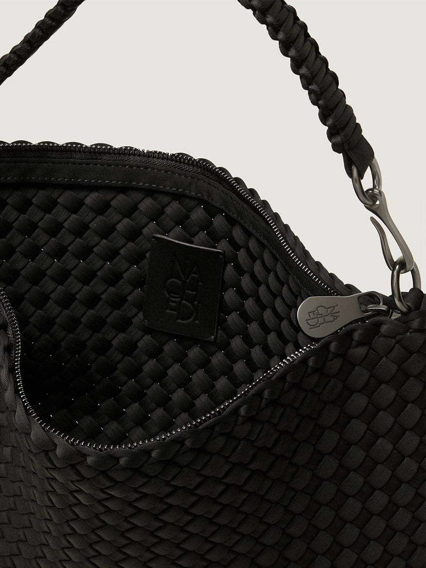 Close-up of the open top of the Naghedi Porto Small Half-Moon Bag in Onyx, showing its black handwoven neoprene exterior, interior lining, black brand tag, and silver zipper.