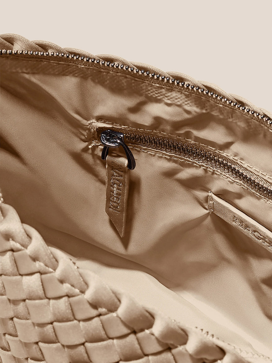 Close-up of a beige handwoven neoprene Naghedi Portofino Cosmetic Clutch in Solid Cashmere with a zipper partially open, revealing the interior fabric and a zipper pull.