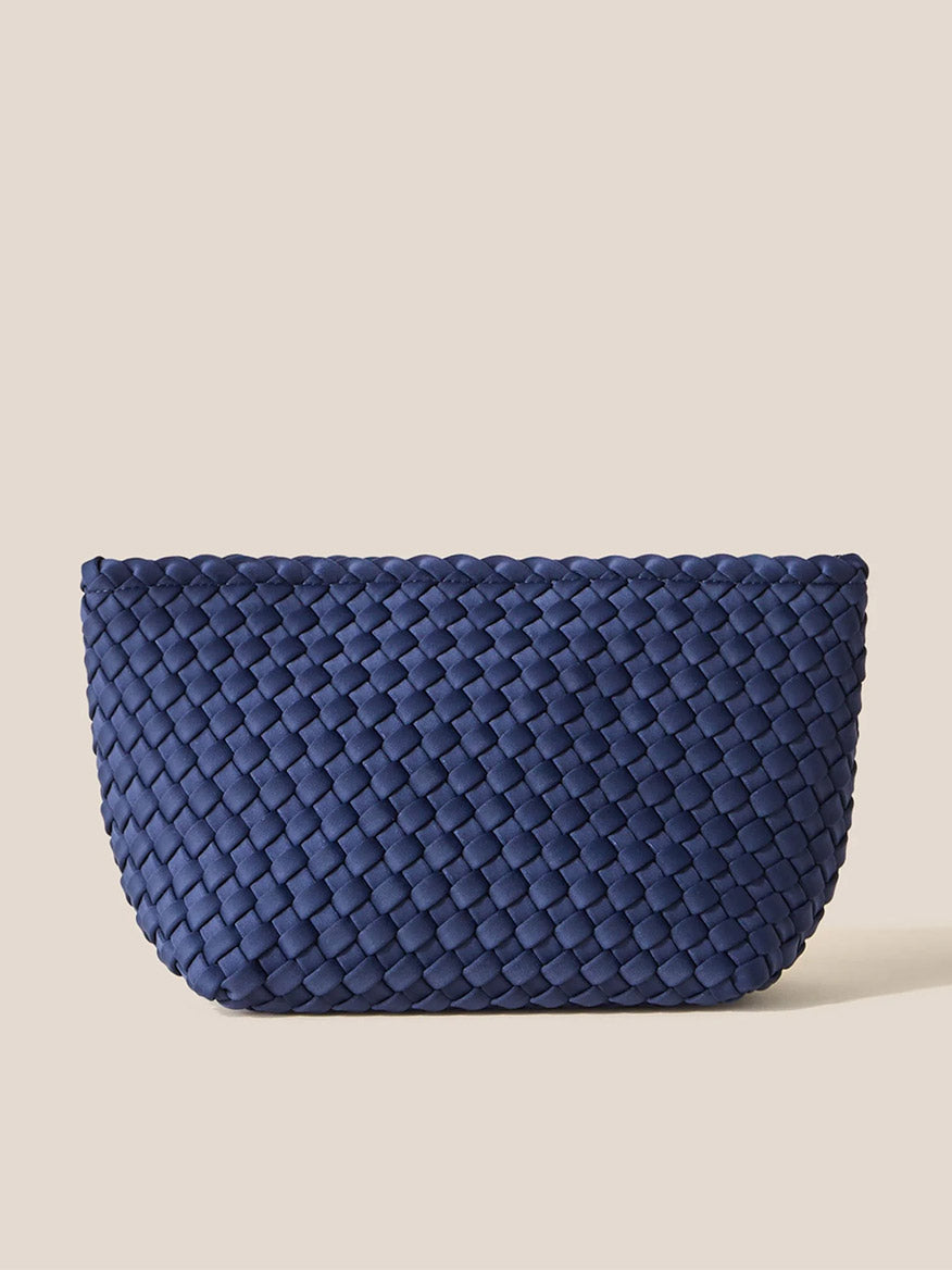 The Naghedi Portofino Cosmetic Clutch in Solid Ink Blue combines style and practicality with its horizontally patterned weave, providing both organization and easy portability. Set against a simple beige backdrop, this handwoven neoprene accessory is a perfect blend of fashion and function.