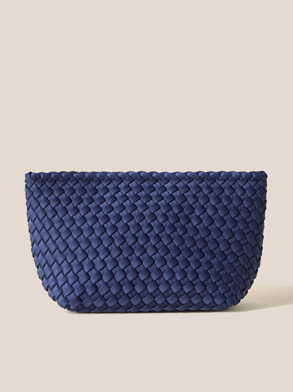 The Naghedi Portofino Cosmetic Clutch in Solid Ink Blue combines style and practicality with its horizontally patterned weave, providing both organization and easy portability. Set against a simple beige backdrop, this handwoven neoprene accessory is a perfect blend of fashion and function.