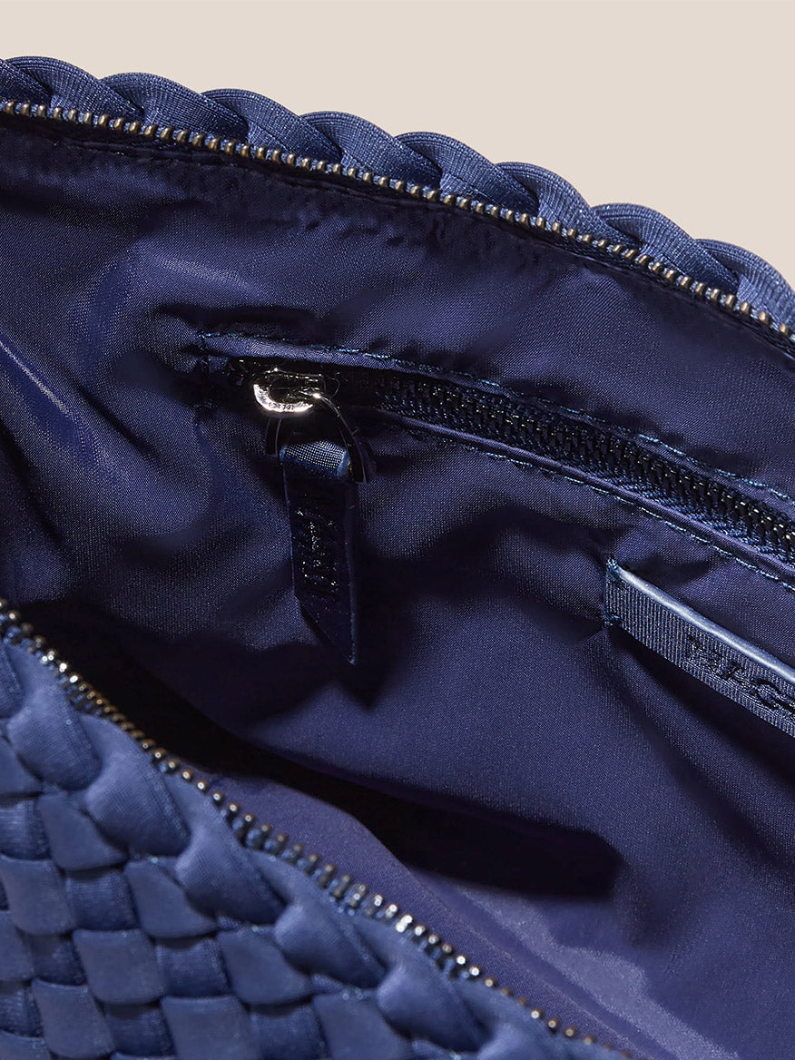 Close-up of the Naghedi Portofino Cosmetic Clutch in Solid Ink Blue, showcasing its open handwoven neoprene design with a dark lining. The clutch includes an interior zippered pocket and a small leather tag, making it ideal for keeping your belongings organized while on the move.