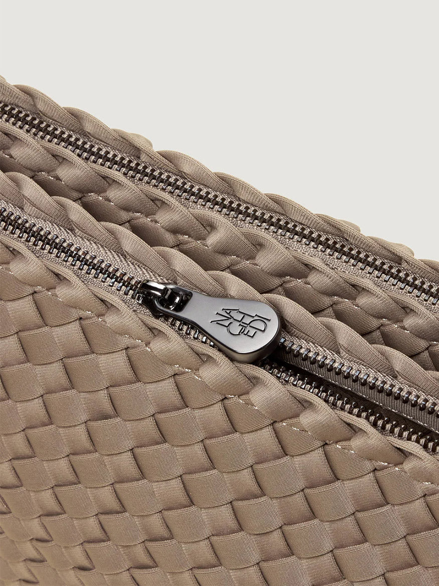 Close-up of the Naghedi Soho Envelope Crossbody in Cashmere, featuring taupe woven neoprene, a visible silver zipper, and a logo-engraved zipper pull.