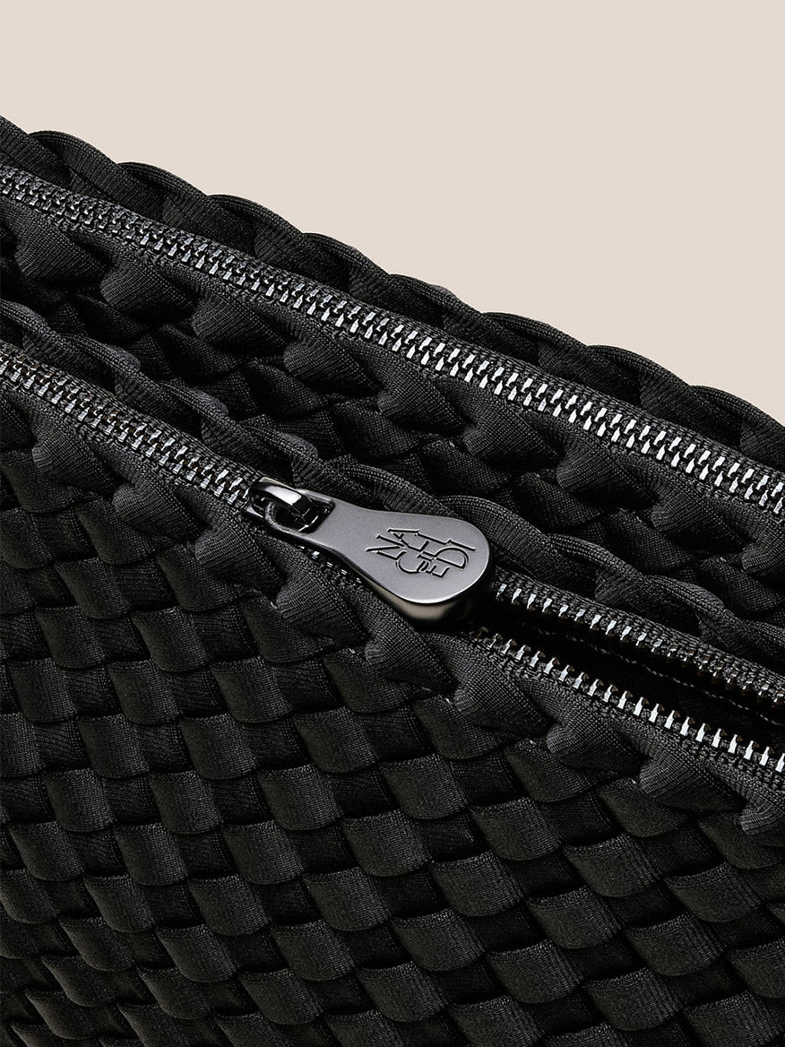 Close-up of the Naghedi Soho Envelope Crossbody in Onyx, featuring black woven neoprene, a silver zipper with branded pull tab, and an adjustable crossbody strap.