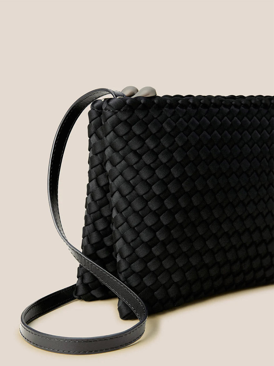 The Naghedi Soho Envelope Crossbody in Onyx is a black woven neoprene bag featuring an adjustable strap and clasp closure, shown against a plain beige background.