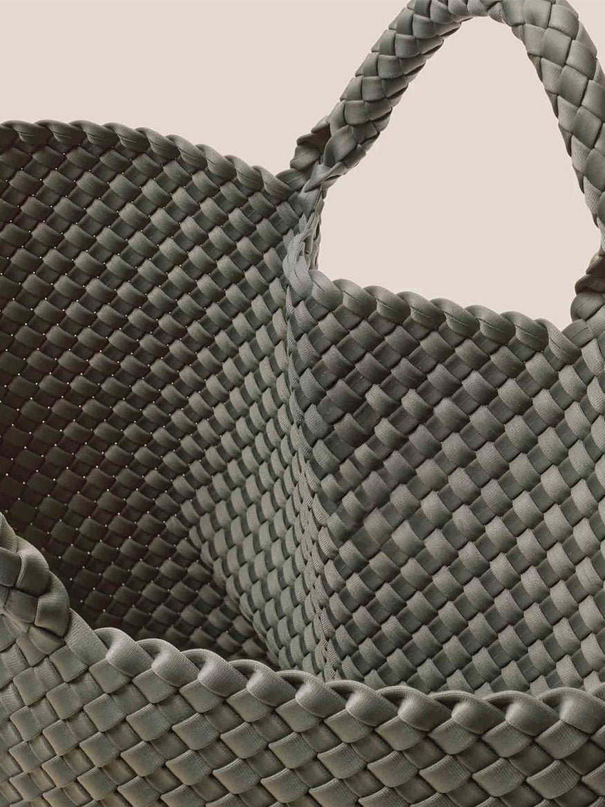 Close-up of a green handwoven neoprene basket with a twisted handle, reminiscent of the craftsmanship seen in the Naghedi St. Barths Large Tote in Solid Laurel, against a beige background.