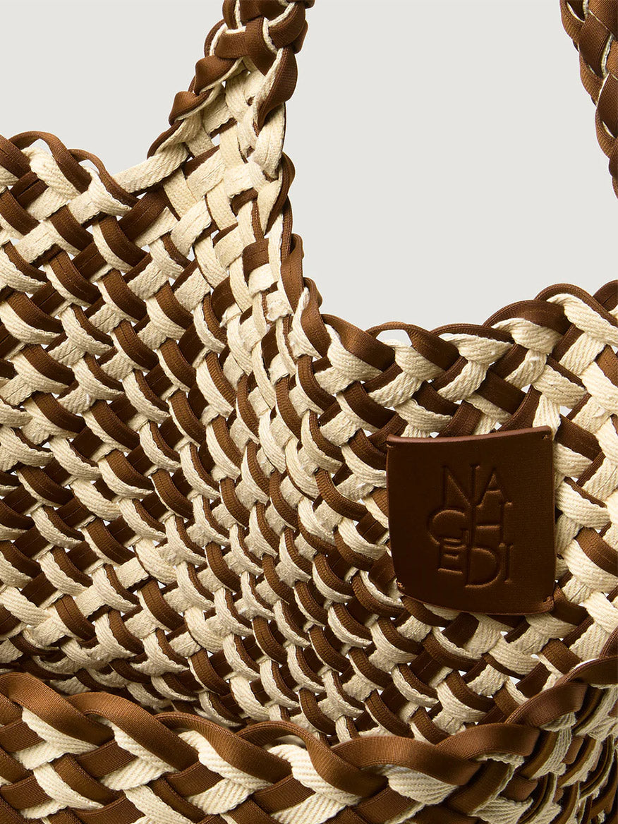 Close-up of the Naghedi St. Barths Medium Tote in Double Weave Carmel—a handwoven neoprene bag in beige and brown with a branded brown leather patch and subtle gold hardware accents.