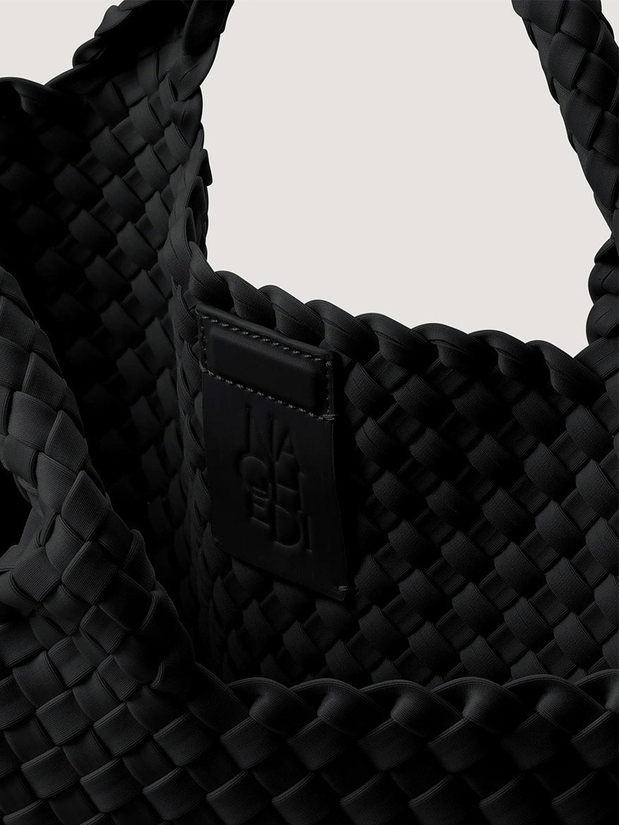 Black woven Naghedi St. Barths Medium Tote in Onyx featuring a centered embossed logo patch on the interior.