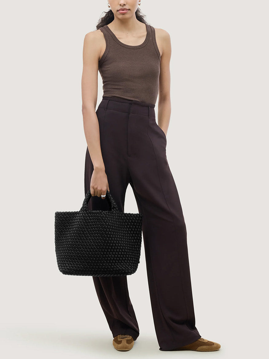 A person holding a black woven Naghedi St. Barths Medium Tote in Onyx.