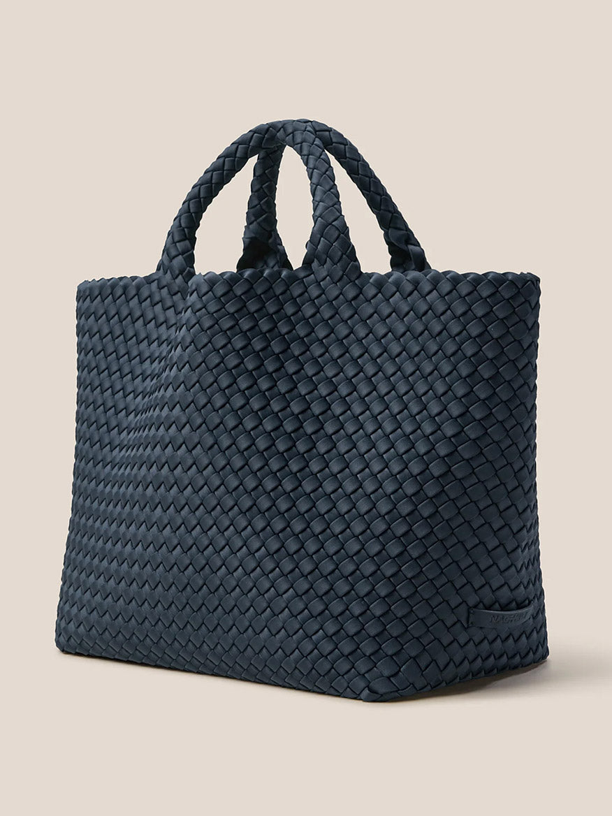 Positioned gracefully on a beige background, the dark handwoven Naghedi St. Barths Medium Tote in Solid Murano showcases its elegant design with two handles. This exquisite tote perfectly combines style and practicality, making it the quintessential everyday accessory for any occasion.