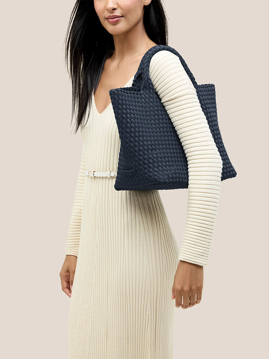 A woman in a white ribbed dress carries a large Naghedi St. Barths Medium Tote in Solid Murano, perfect for everyday use, slung over her shoulder.