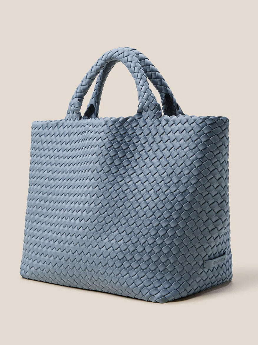 The Naghedi St. Barths Medium Tote in Solid Nova is an everyday bag crafted from handwoven neoprene, displaying a vibrant blue shade and featuring two sturdy handles on a neutral background.