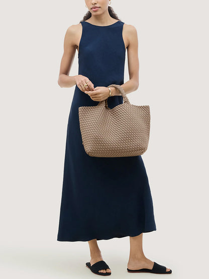 A person in a navy blue dress holds a medium-sized beige handwoven Naghedi St. Barths Medium Tote in Cashmere.