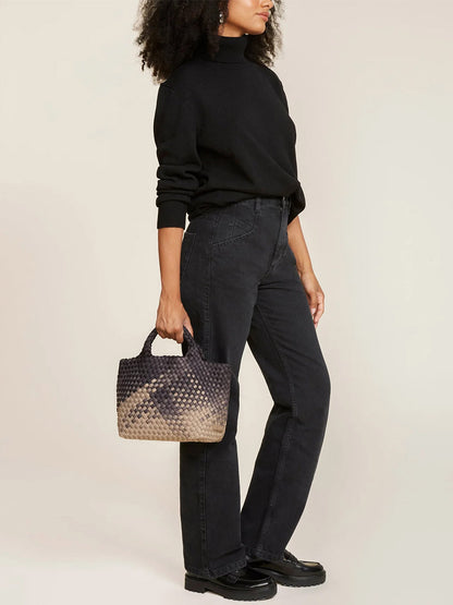 A woman wearing black pants and a black sweater carrying a Naghedi St. Barths Mini Tote in Graphic Ombre Mahal.