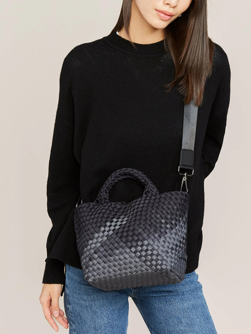 A woman in a black sweater carrying a large handwoven Naghedi St. Barths Small Tote in Graphic Ombre Basalt.
