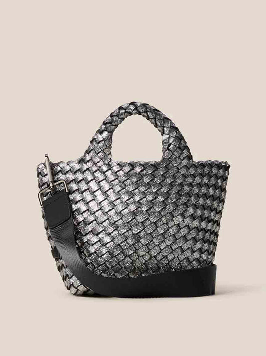 The Naghedi St. Barths Petit Tote in Metallic Titanium is crafted from handwoven neoprene and features short handles, along with a wide black crossbody strap. Set against a plain background, it exudes modern sophistication.