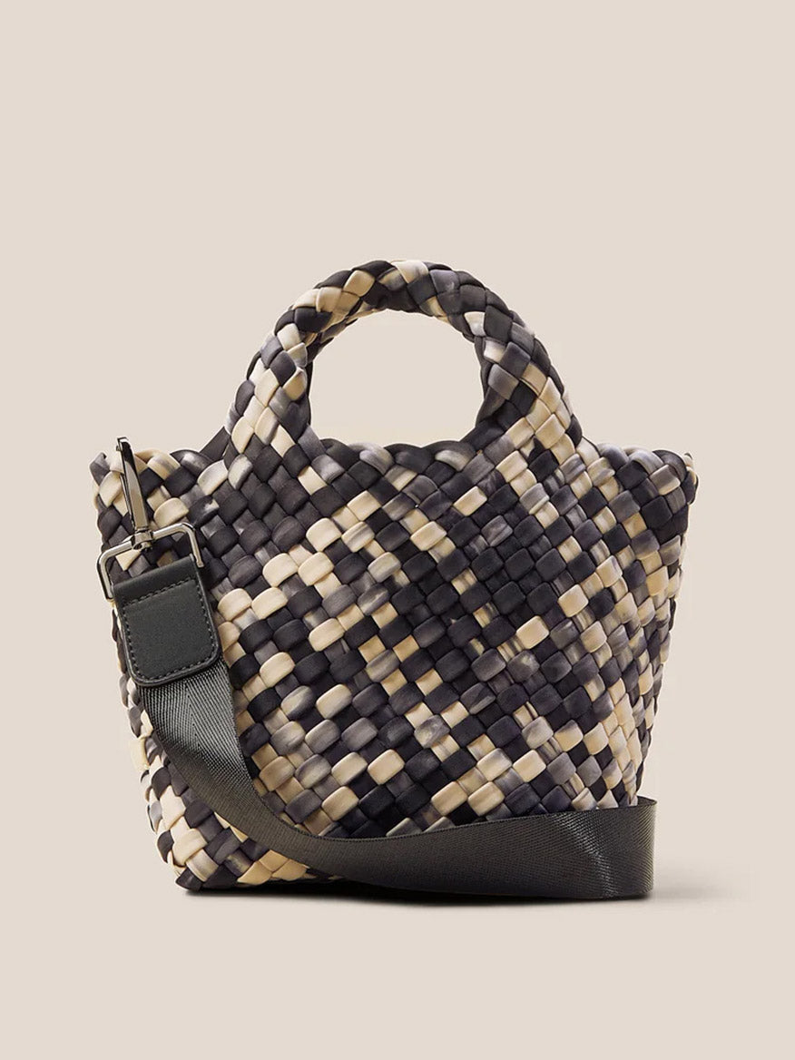 The Naghedi St. Barths Petit Tote in Watercolor Nimbus is a handwoven neoprene handbag showcasing a black, beige, and gray checkered pattern. It includes a short handle and an adjustable black strap that transforms into a detachable crossbody strap for versatile styling choices.