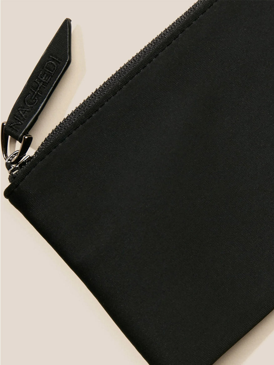 Close-up of a black fabric pouch, showcasing a visible zipper and a leather pull tag embossed with "NAGHEDI." It captures the sophisticated charm of the Naghedi St. Barths Petit Tote in Watercolor Nimbus, enhanced by its handwoven neoprene detailing for added texture.