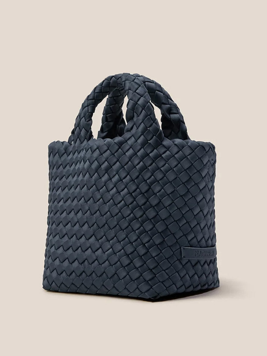 The Naghedi St. Barths Petit Tote in Solid Murano is a dark, handwoven neoprene handbag with two handles, elegantly displayed against a neutral background.