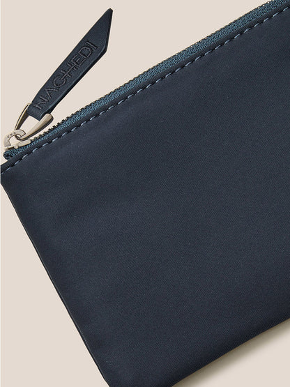 Close-up of a Naghedi St. Barths Petit Tote in Solid Murano, featuring a navy blue zippered pouch with a branded leather pull tab and an optional crossbody strap, set against a neutral background.