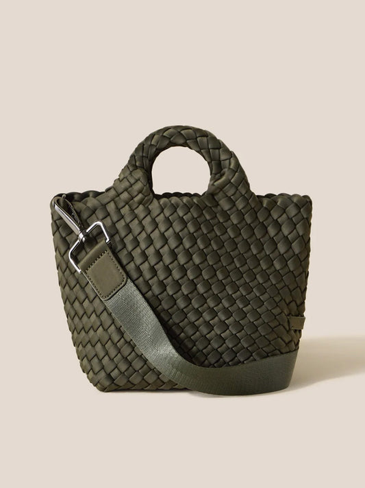 The Naghedi St. Barths Petit Tote in Solid Olive showcases a handwoven neoprene design in green, complemented by a short handle and an adjustable crossbody strap on a neutral backdrop.