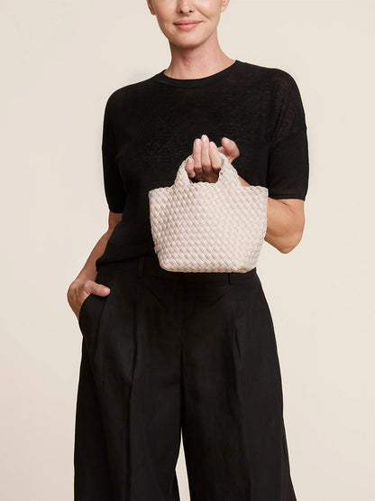 Woman holding a Naghedi St. Barths Petit Tote in Solid Shell Pink while wearing a black outfit.
