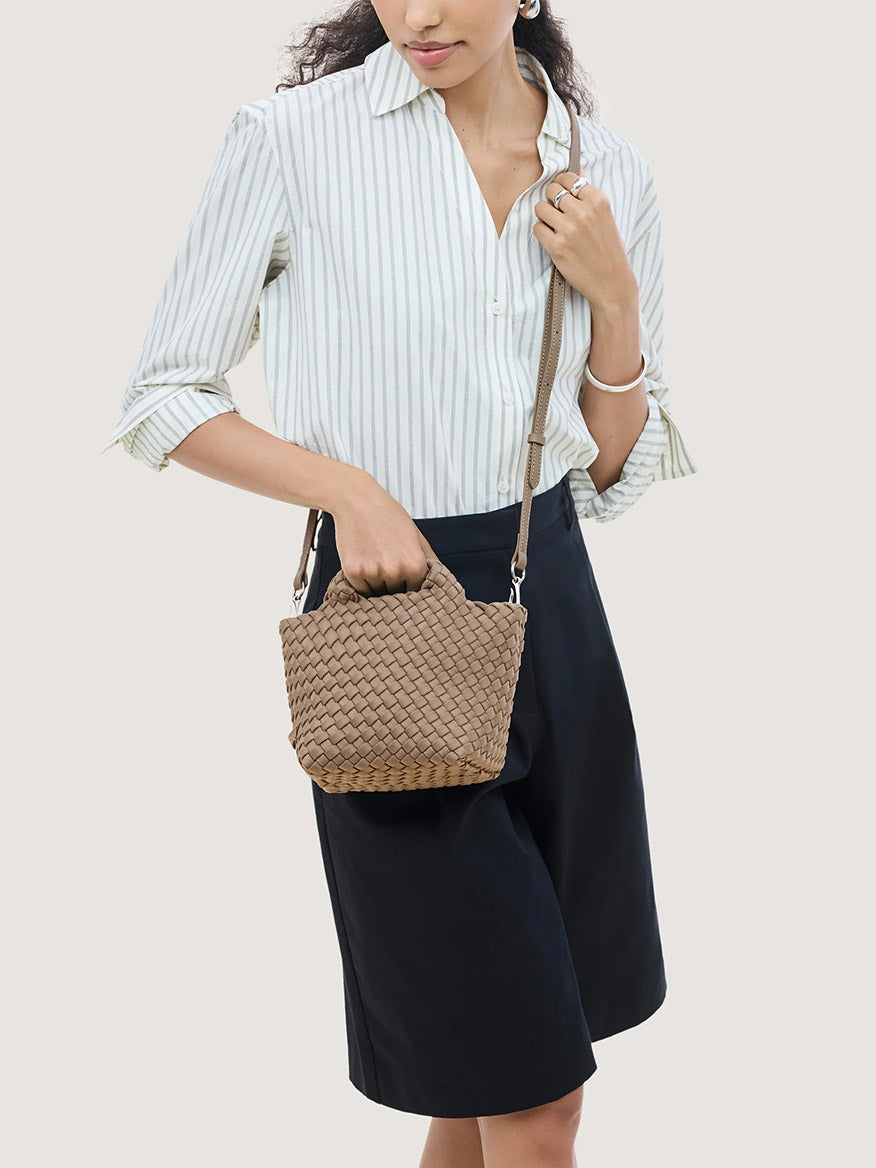 A person holds a small, taupe-colored, handwoven neoprene Naghedi St. Barths Petit Tote in Cashmere with a detachable shoulder strap.