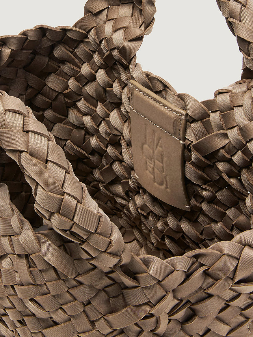 Close-up of a taupe handwoven neoprene Naghedi St. Barths Petit Tote Nest Weave in Cashmere featuring an interior embossed brand patch.