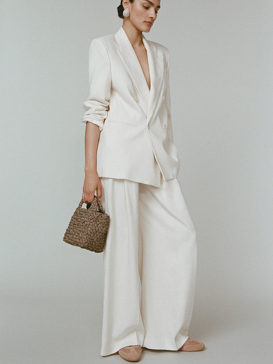 A model in a cream-colored pantsuit holds a taupe Naghedi St. Barths Petit Tote Nest Weave in Cashmere.